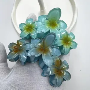 Dettaglio della molletta per capelli a fiori di plumeria blu sfumato su base bianca