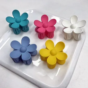 Dettaglio di cinque mollette per capelli a fiore opaco in colori pastello su vassoio bianco