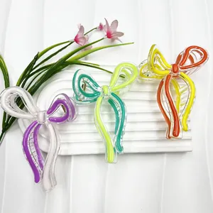 Three colorful acrylic bow hair claws in purple, green, and orange on a white wave plate