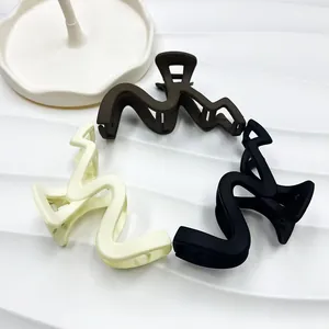 Drei matte Haarklammern in Schwarz, Creme und Kaffee auf einem weißen Wellenhintergrund