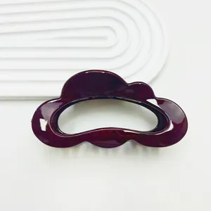 Glossy burgundy hair claw clip with cloud-like wave design on white textured background