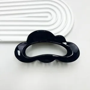 Macro detail of a glossy black cloud-shaped hair claw clip on a white textured tray