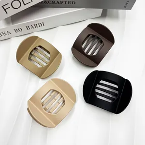 Close-up of four matte-finish flat round hair clips in black, brown, and beige tones