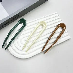 Detailed view of U-shaped hairpins in dark green, cream, and brown on a tray
