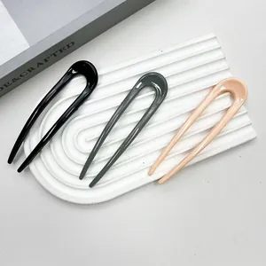 Close-up of three U-shaped hairpins in black, grey, and nude pink on a white textured base