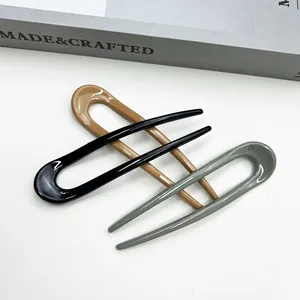Close-up of three glossy U-shaped hairpins in black, amber, and grey-green colors