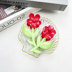 Dettaglio di due mollette per capelli a fiore rosso con foglie verdi su vassoio