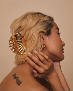 Detalle de la pinza de pelo plisada dorada y pendientes de tuerca en un modelo