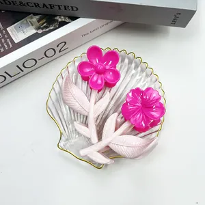 Dettaglio di pinze per capelli a fiore rosa con manici a foglia in un piatto di vetro
