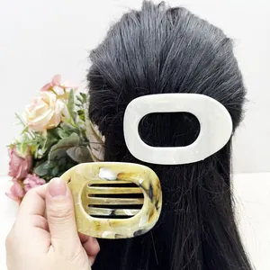 Détail de la pince à cheveux motif marbre tenue en main et portée sur cheveux lisses