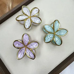 Detail of three frangipani hair claws with gold edges and crackle finish texture