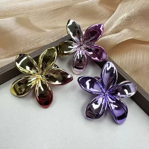 Close-up of three electroplated frangipani hair clips in gold and purple metallic finishes