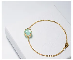 Detail van gouden armband met een gefacetteerd lichtgroen kristal in een stevige klauwzetting
