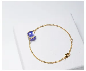 Detail van gouden armband met een vierkante blauwe kristal in een vierklauwzetting