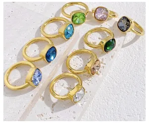 Detail view of nine square-cut colorful crystal rings on a white stone surface