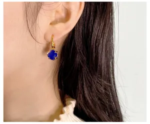 Detail eines goldenen Leverback-Ohrrings mit facettiertem dunkelblauem Kristall am Model