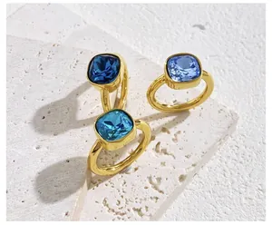 Detail of square-cut crystal rings in blue and teal with a polished gold finish band