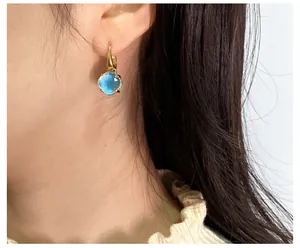 Nahaufnahme eines goldenen Ohrrings mit rundem himmelblauem Kristall am Modell
