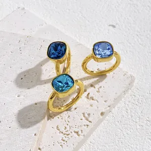 Three-piece set of square blue crystal rings with golden plating on a stone surface