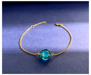 Detail van de gouden kettingarmband met een facetgeslepen blauw kristal en karabijnsluiting