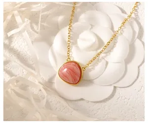 Detail of a gold necklace featuring a triangular pink gemstone on a white flower backdrop