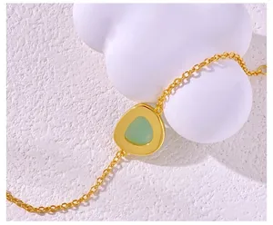 Macro detail of a gold chain bracelet featuring a green gemstone in a metal pendant