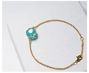Detail van een gouden armband met een gefacetteerd blauw kristal en een handige karabijnsluiting