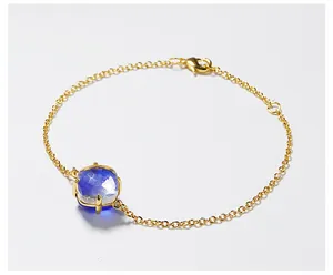 Detailopname van gouden kettingarmband met gefacetteerd blauw kristal en een karabijnsluiting