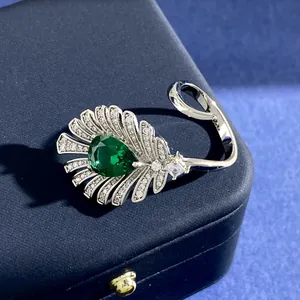 Makrofoto eines Pfauenfeder-Rings mit grünem birnenförmigem Edelstein und Diamanten