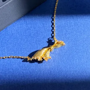 Brushed gold bow necklace with micro-pave diamonds on navy blue background