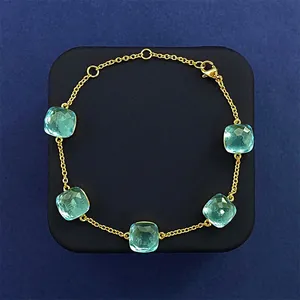 Macro detail of gold-plated bracelet featuring five cushion-cut light blue gemstones