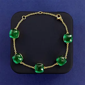 Detail of green emerald-cut crystal stones on a gold chain bracelet with lobster clasp