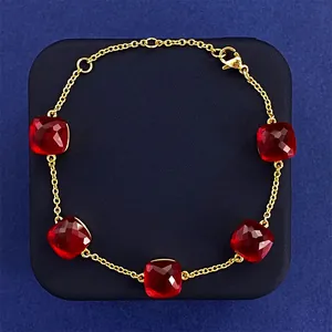 Detail view of gold chain bracelet with five square red crystals and lobster clasp