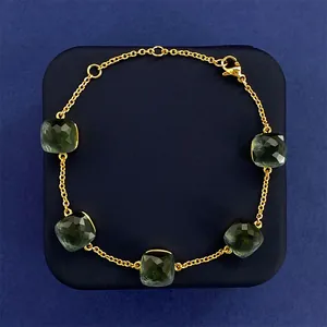 Macro shot of gold bracelet featuring five square-cut green gems with lobster clasp detail