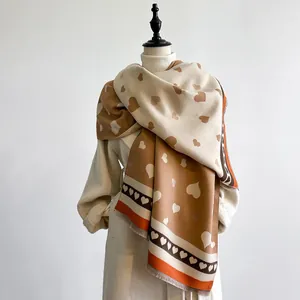 Detail eines Herzmuster-Strickschals mit weichen Fransen und warmem Beige-Khaki-Farbschema