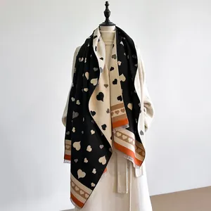 Detail eines dicken beidseitigen Winterschals mit Herzmustern und orangefarbenen Quasten