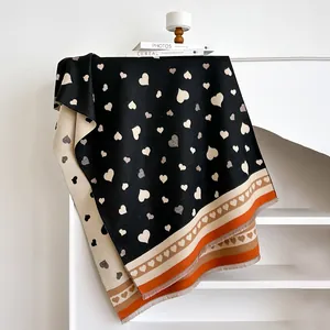 Detail eines doppelseitigen Herzmuster-Strickschals mit orangefarbenen Streifen und Fransen