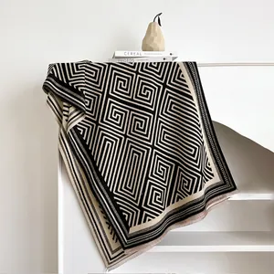 Detail of cashmere-like scarf showing geometric Greek key pattern and soft fringe edges