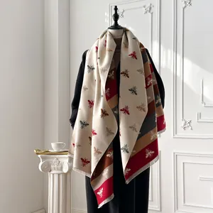 Close-up of thick beige cashmere-feel shawl with bee print and striped fringe hem