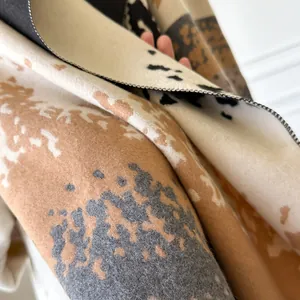 Close-up of thick winter scarf showing soft cow print plush fabric and hemmed edges