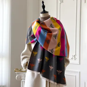 Detail of soft faux cashmere scarf with colorful stripes and bee patterns and tassels