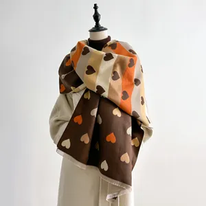 Detail of soft cashmere-feel scarf featuring colorful heart patterns and fringe edges
