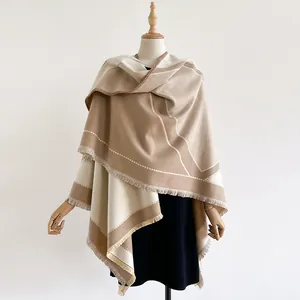Detailed macro view of the thick cashmere-like shawl featuring soft tassels and geometric blocks
