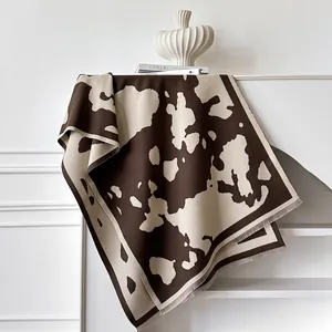 Écharpe style cachemire à motif vache marron avec franges sur support décoratif