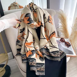 Floral shawl scarf in beige with orange flower pattern and tassel edges on a chair