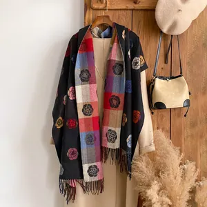 Detail of floral cashmere-like scarf with fringe hanging on wooden hanger and beige coat