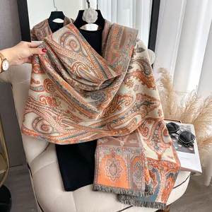Détail des motifs cachemire et franges douces sur un châle d'hiver orange et gris