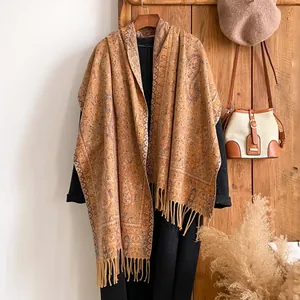 Dettaglio di scialle vintage con motivi paisley e frange su cappotto autunnale