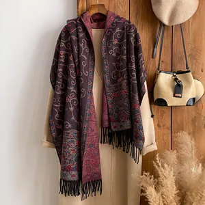 Detail of vintage floral paisley scarf with long tassels draped over a beige winter coat