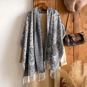 Dettaglio dello scialle vintage con motivo paisley e frange su un cappotto beige